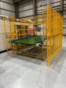 Esteira transportadora horizontal com gaiola de proteção amarela e sensores de segurança para área de robô em conformidade com a NR-12.